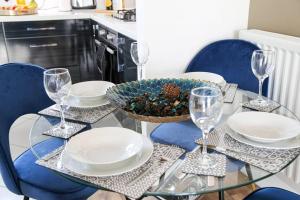 a glass table with plates and wine glasses on it at Luxury Apartment with Balcony, Fast WIFI, Smart TVs and Free Parking by Yoko Property in Milton Keynes