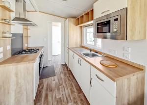cocina con armarios blancos, fregadero y microondas en Towervans Caravan Park en Mablethorpe
