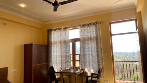 Happy home stay, Dharamshala في دارامشالا: غرفة مع نافذة كبيرة مع طاولة وكراسي