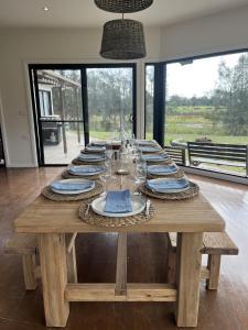 una larga mesa de madera con platos y vasos. en The Ranch - Coastal Farmhouse midway to Newcastle Airport and Beaches en Salt Ash