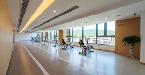 Un gimnasio con cintas de correr y elípticas en una sala grande con ventanas. en Hentique Manna Tangshan, en Nanjing