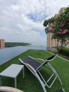 einen Stuhl und einen Tisch auf einer Wiese mit Blick auf das Wasser in der Unterkunft Seaview Infinity Retreat Urban Suite 3R2B 8Pax Georgetown in Jelutong