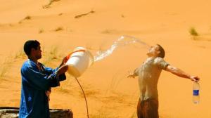 Deux hommes se tenant dans le désert de l'eau potable provenant d'un seau dans l'établissement Camels House, à Merzouga