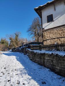 a snow covered street next to a stone building at Расимова къща in Bozhentsi