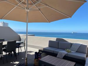 eine Terrasse mit einem Sofa und einem Sonnenschirm und dem Meer in der Unterkunft Coastal Hospitality - De Valle 65 in Mossel Bay