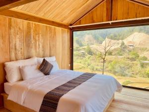 a bed in a wooden room with a large window at Na Thẩm Eco Hill Homestay - Trạm Tấu in Cham Ta Lao