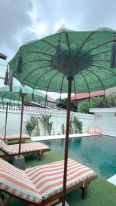 a pool with two lounge chairs and a green umbrella at Kaktus Boutique Apartments Bali - ADULTS RETREAT in Legian
