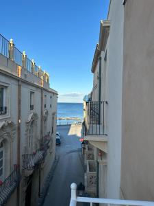an alley with buildings and the ocean in the background at Archè in Syracuse