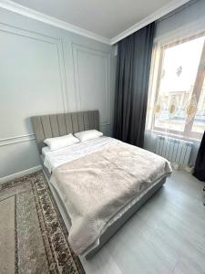 a bed in a bedroom with a large window at Keruen Saray Apartments 2 in Türkistan