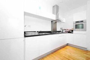 a white kitchen with white cabinets and a wooden floor at Modern 2 Bed, 2 Bath Flat in Central London Zone 1 in London