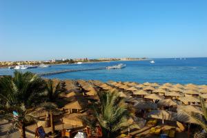 - un groupe de parasols en paille sur une plage au bord de l'eau dans l'établissement Jaz Makadi Saraya Palms, à Hurghada