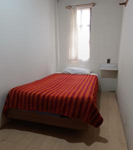 a bed in a white room with a red striped blanket at Hostal Casona Don Ranulfo in Peñas