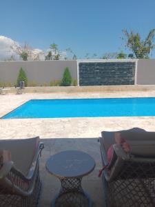 una mujer sentada en sillas junto a una mesa junto a una piscina en Villa Ada Luxury Retreat en Juan Dolio