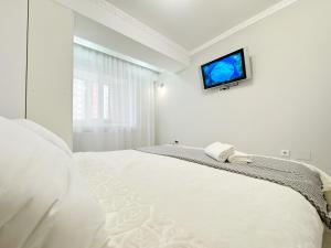 a white bedroom with a bed with a tv on the wall at Gio Apartment in Chişinău