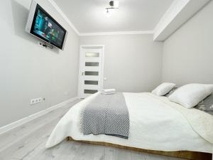 a white bedroom with a bed and a tv on the wall at Gio Apartment in Chişinău