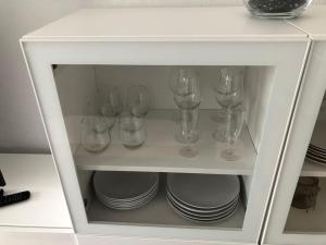un armario blanco con vasos y platos. en Schwarzwald Apartment mit Terasse, en Schönwald
