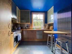 a kitchen with blue walls and wooden cabinets and a table at 8 Ravenscourt Gardens in London