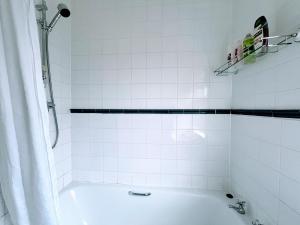 ein weiß gefliestes Bad mit einer Badewanne und einer Dusche in der Unterkunft 1 Lathom Ave - Parking, 2 Bathrooms, Comfortable, Welcoming, Nice Area in Morecambe