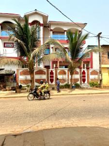 dos personas conduciendo una motocicleta por una calle frente a un edificio en Luxe 3 Ch.Apt Porto Novo,Abgokou en Porto-Novo