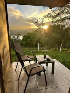 un patio con 2 sillas, una mesa y la puesta de sol en LakeLifeCR Tu casa frente al Lago Arenal, en Tilarán