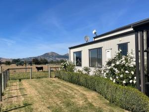 a house with a fence and a cow in a field at The Barn in Mosgiel