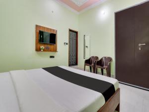 a bedroom with a bed with two chairs and a tv at OYO Shri Radhe Guest House & Restaurant in Rishīkesh