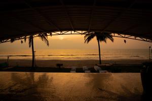 a sunset at the beach with chairs and palm trees at Beach House Resort Goa in Benaulim