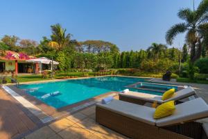 uma piscina com um sofá e uma cadeira ao lado em Moksh Villa by StayVista - Amidst of orchards, with a pool, gazebo, and indoor games em Alibaug