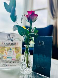 un jarrón de cristal con una rosa y un libro sobre una mesa en Hotel No5, Beachfront with Free Private Car Park en Llandudno