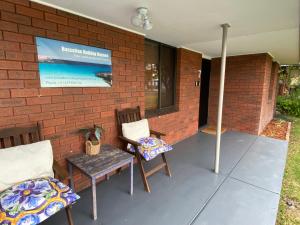 a patio with two chairs and a sign on a brick wall at Abbey Beach Shack in Busselton