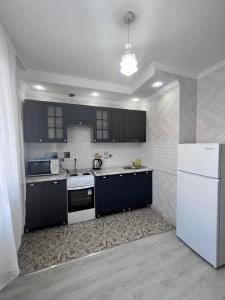 a kitchen with black cabinets and a white refrigerator at Классная квартира у Almaty Arena 93-62 in Almaty