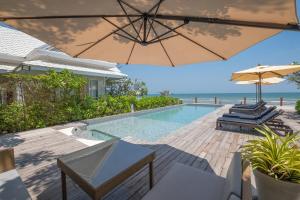 uma piscina com guarda-sol e cadeiras e o oceano em De Chaochom Hua Hin em Hua Hin