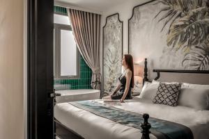 a woman sitting on a bed in a hotel room at T-Maison Indochine Vung Tau Villa near beach with pool, billiards, karaoke in Vung Tau