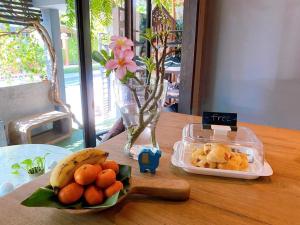 a wooden table with a bowl of oranges and a container of fruit at To Bed Poshtel in Chiang Mai