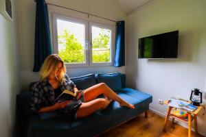 a woman sitting on a couch reading a book at Tinyhouse „Kleines Ems-Idyll“ in Lathen