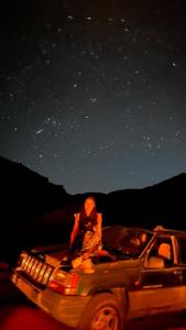 a man sitting on the back of a car under the stars at Experience sleep under the star in Wadi Rum