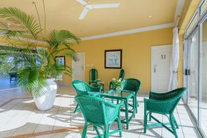 Albatross Guesthouse في ساوثبروم: غرفة طعام بها كراسي خضراء وطاولة والنخيل