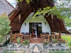 ein Haus mit einem Strohdach und Stühlen davor in der Unterkunft Sumatra Orangutan Treks Villa in Timbanglawang