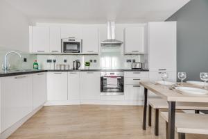 a kitchen with white cabinets and a wooden table at Modern 1 BR apt near town centre by Tent serviced apartments in Egham