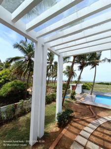 a white pergola with a swimming pool and palm trees at Beach wave villa in Tirupporūr