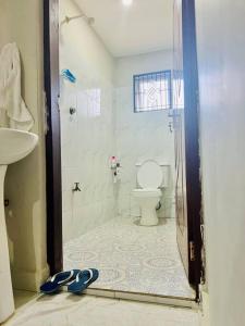 ein Bad mit einer Dusche, einem WC und einem Paar Hausschuhen in der Unterkunft Autumn House DIani in Ukunda