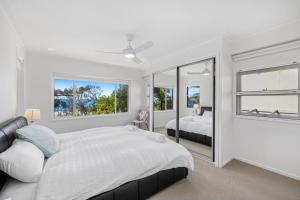 a white bedroom with a bed and two windows at The Sandcastle - 4 Bedroom House in Woolgoolga