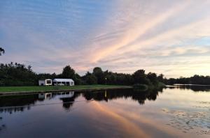 una casa junto a un lago con un arco iris en el cielo en Camping de Kleine Wielen, en Leeuwarden