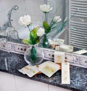 a bathroom counter with a vase with white flowers in it at Logis Hotel-Restaurant Dimmer in Wallendorf pont