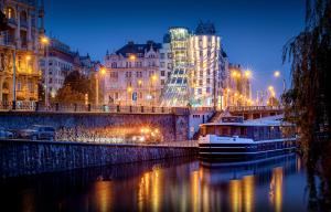 una barca sul fiume in una città di notte di Dancing House - Tančící dům hotel a Praga