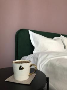una taza de café sentada en una mesa junto a una cama en Saulės Tako apartamentai, en Druskininkai