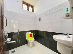 a bathroom with a toilet with a green and red bucket on it at Mango Villa in Varkala