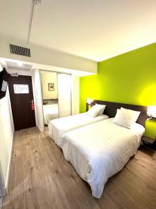 a bedroom with two beds and a green wall at Hôtel Le Cousture in Toulouse