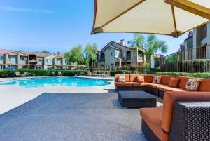 eine Terrasse mit einem Sofa und einem Sonnenschirm neben einem Pool in der Unterkunft CozySuites TPC Scottsdale with parking, pool in Scottsdale