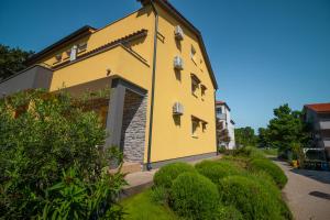 un bâtiment jaune avec des buissons devant lui dans l'établissement Apartments Gracia, à Baška